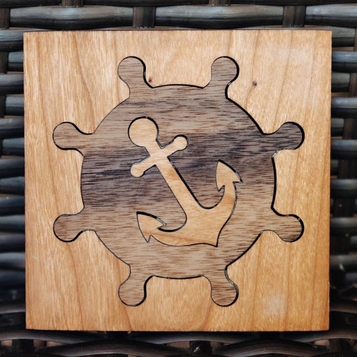 A square wooden plaque featuring an engraved nautical design of a ship's wheel and anchor