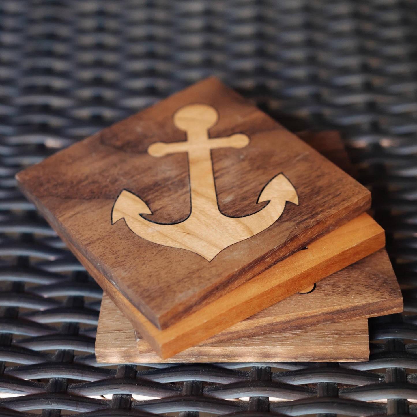 A stack of square wooden coasters with a laser-cut anchor design on the top coaster