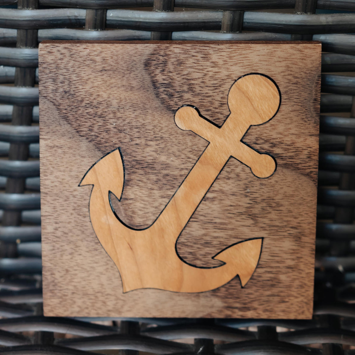 A square wooden plaque featuring an anchor cutout in a lighter natural wood tone