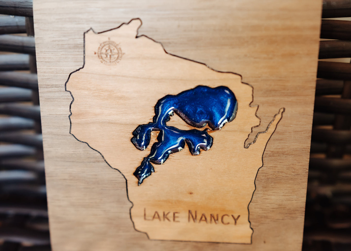 A close-up of a wooden plaque featuring an engraved outline of Wisconsin with a glossy blue Lake Nancy inlay and the words 'LAKE NANCY' engraved at the bottom.
