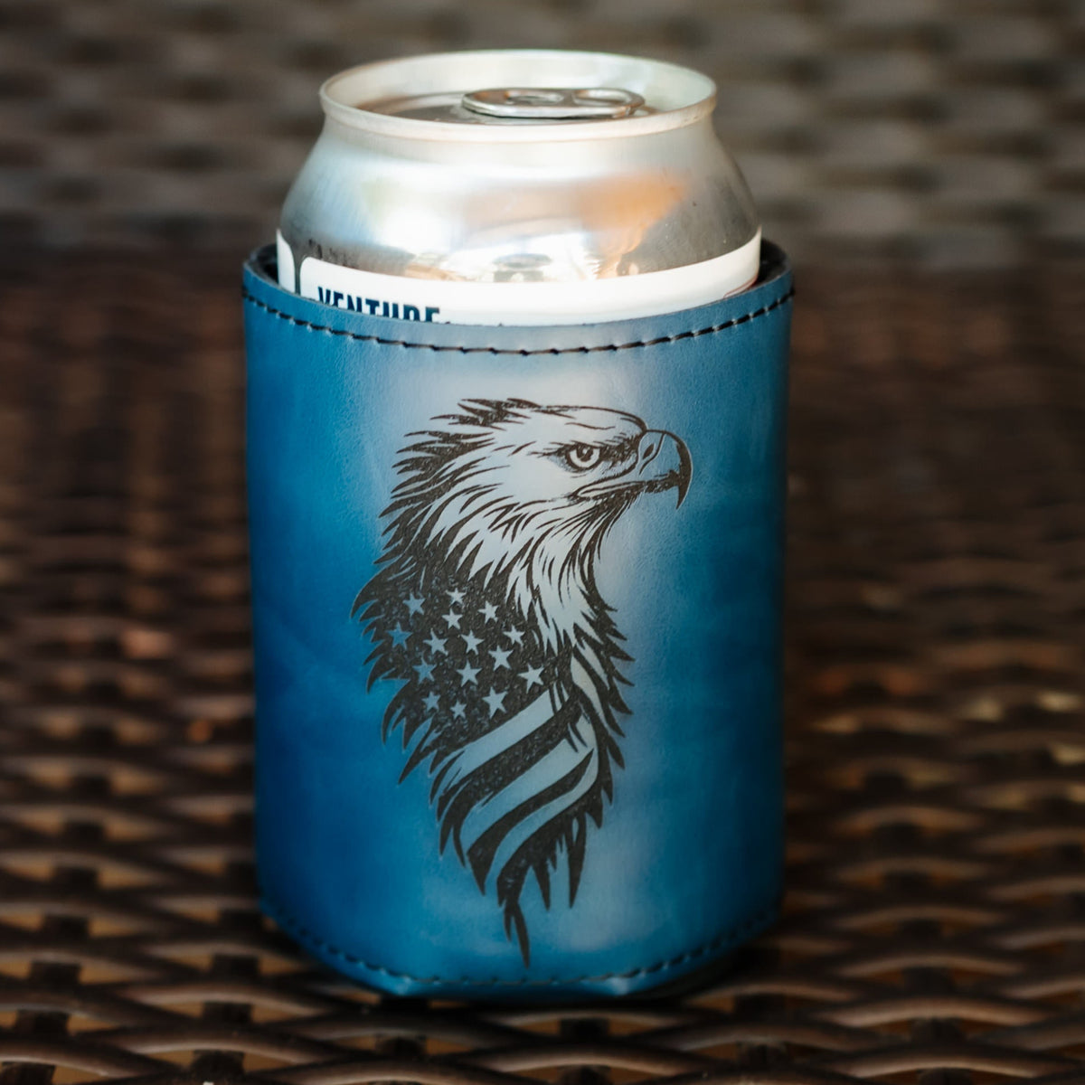A blue insulated can cooler sleeve with a black eagle graphic and American flag pattern